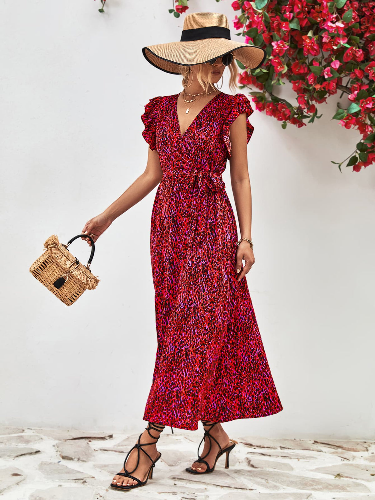 Model wearing red printed long dress, holding a small woven handbag.
