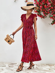 Model wearing red printed long dress, holding a small woven handbag.