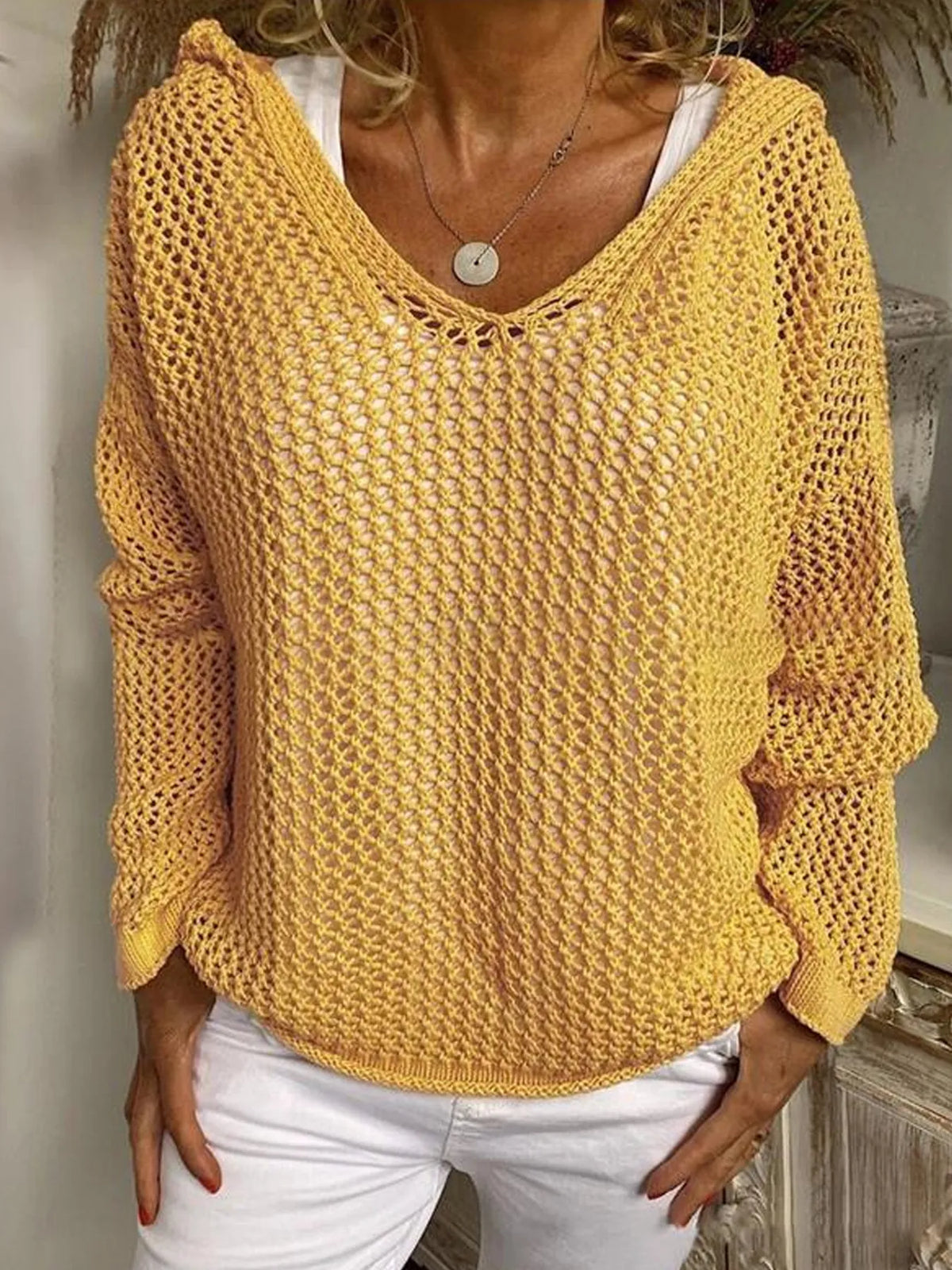 Mustard yellow open-knit hooded cover-up with long sleeves and a V-neck, worn over a white top.