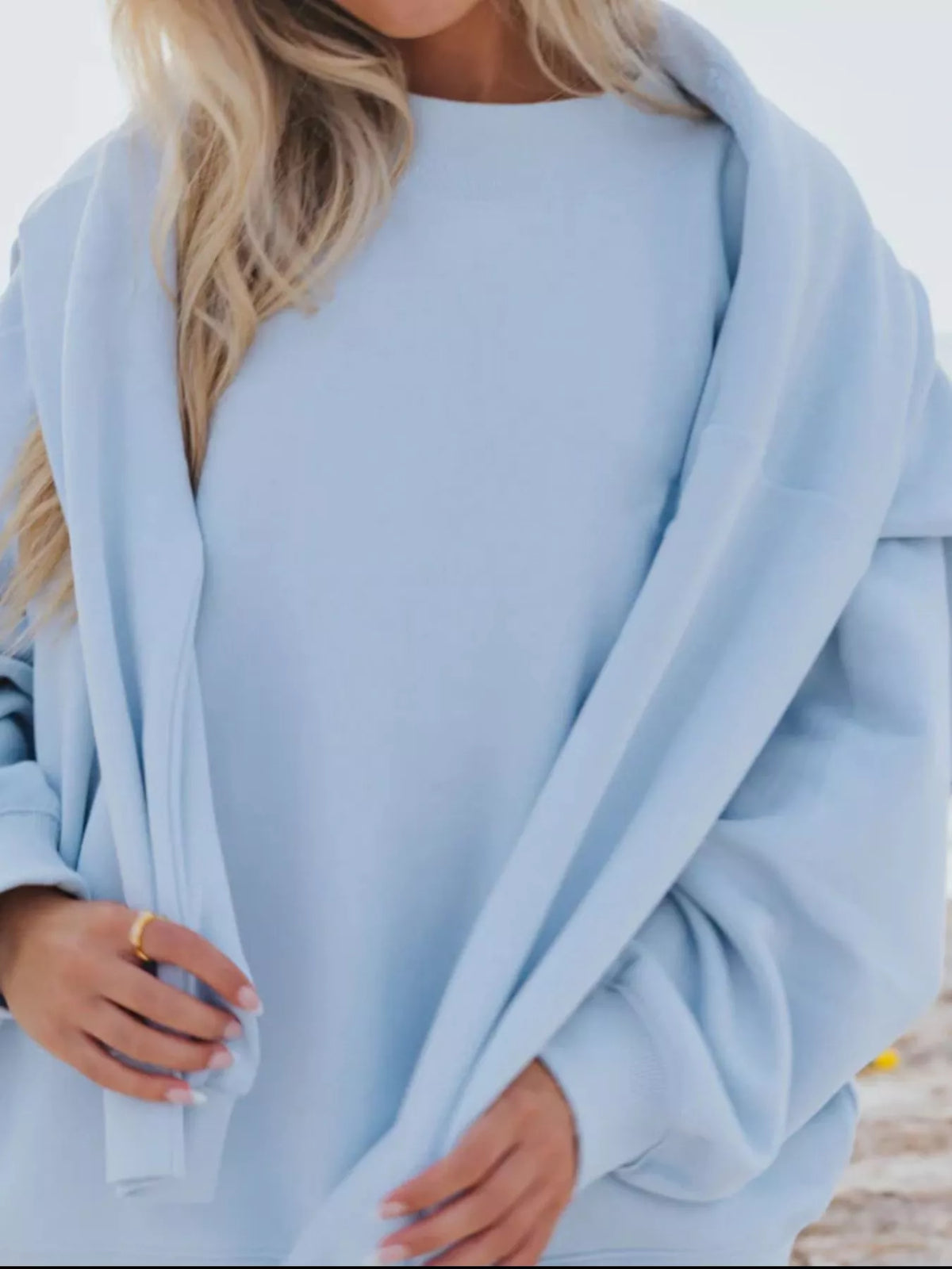 Close view of a light blue oversized sweatshirt held outward at both sides.
