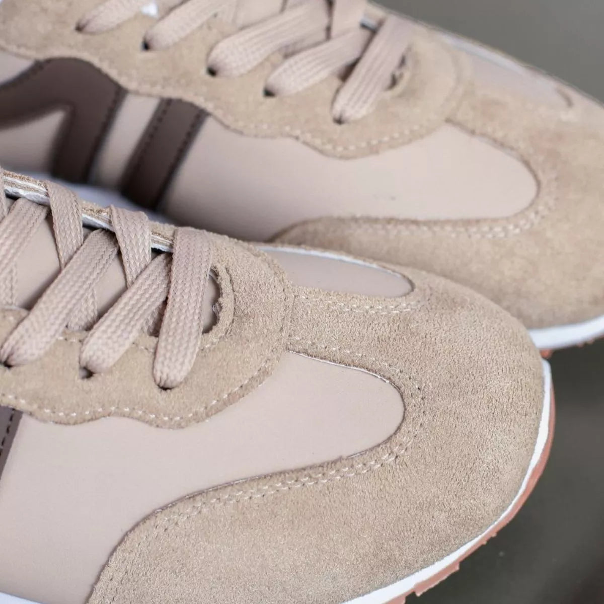 Close view of beige sneaker laces, suede-like toe and contrasting side stripe