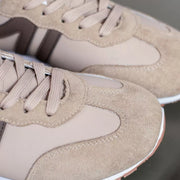 Close view of beige sneaker laces, suede-like toe and contrasting side stripe