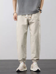 Front view of light beige joggers with drawstring waist, straight legs and elastic ankle cuffs.
