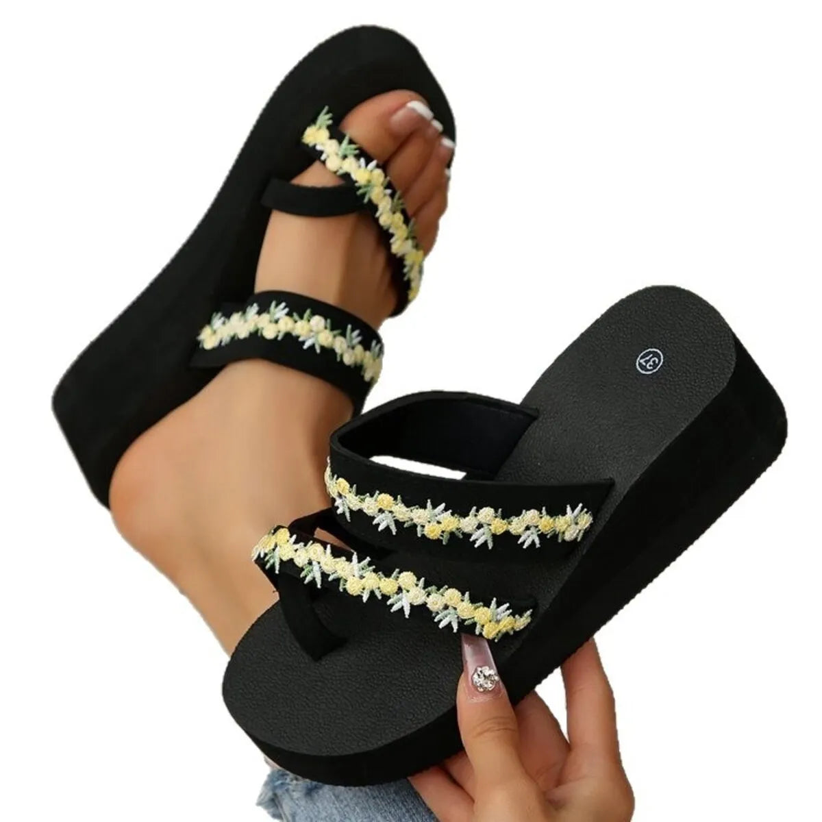 Black platform sandal with pale yellow floral-trim straps held beside a matching worn sandal