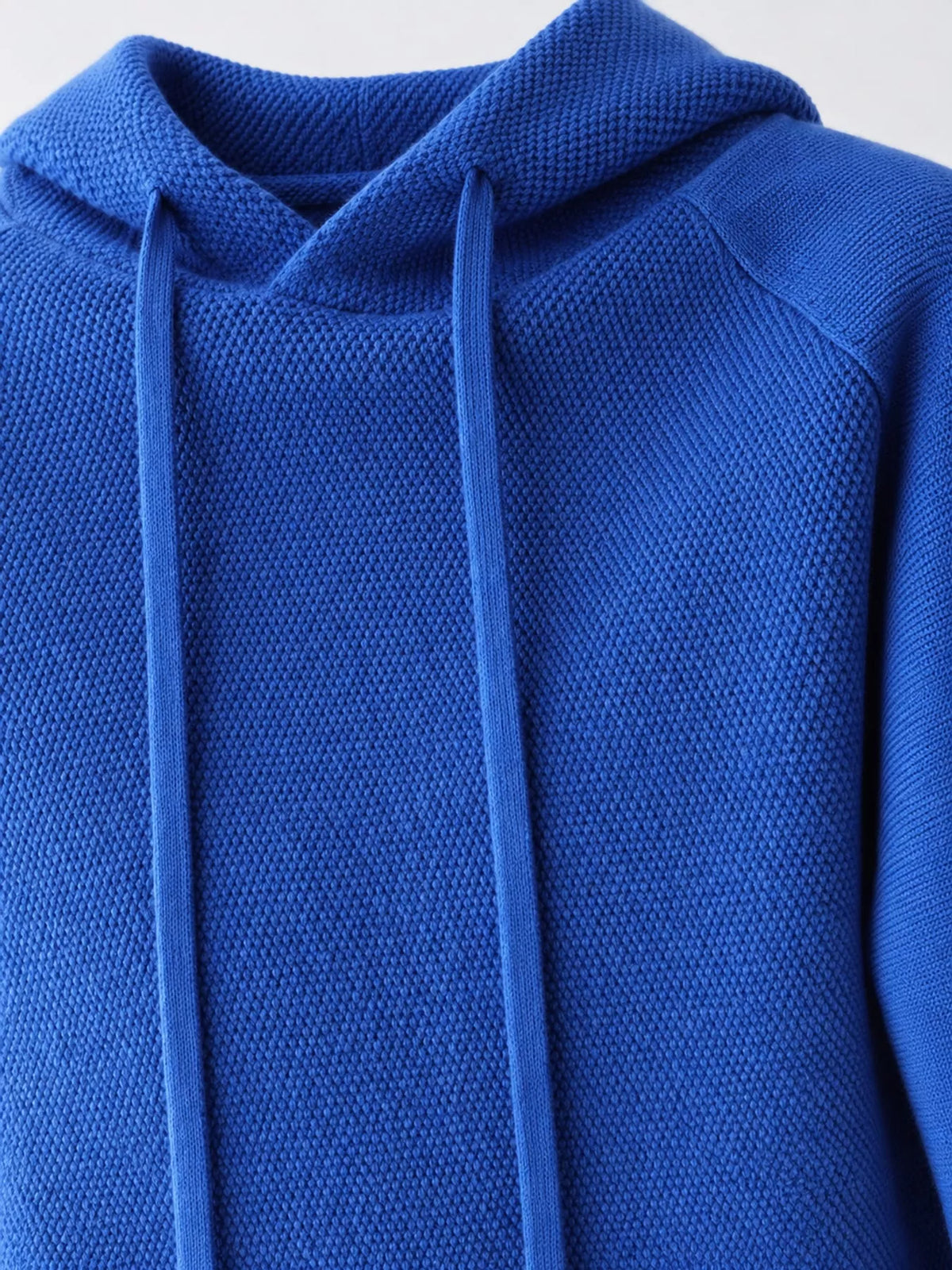 Royal blue sweater close-up showing the hood opening, textured knit and long drawstrings.