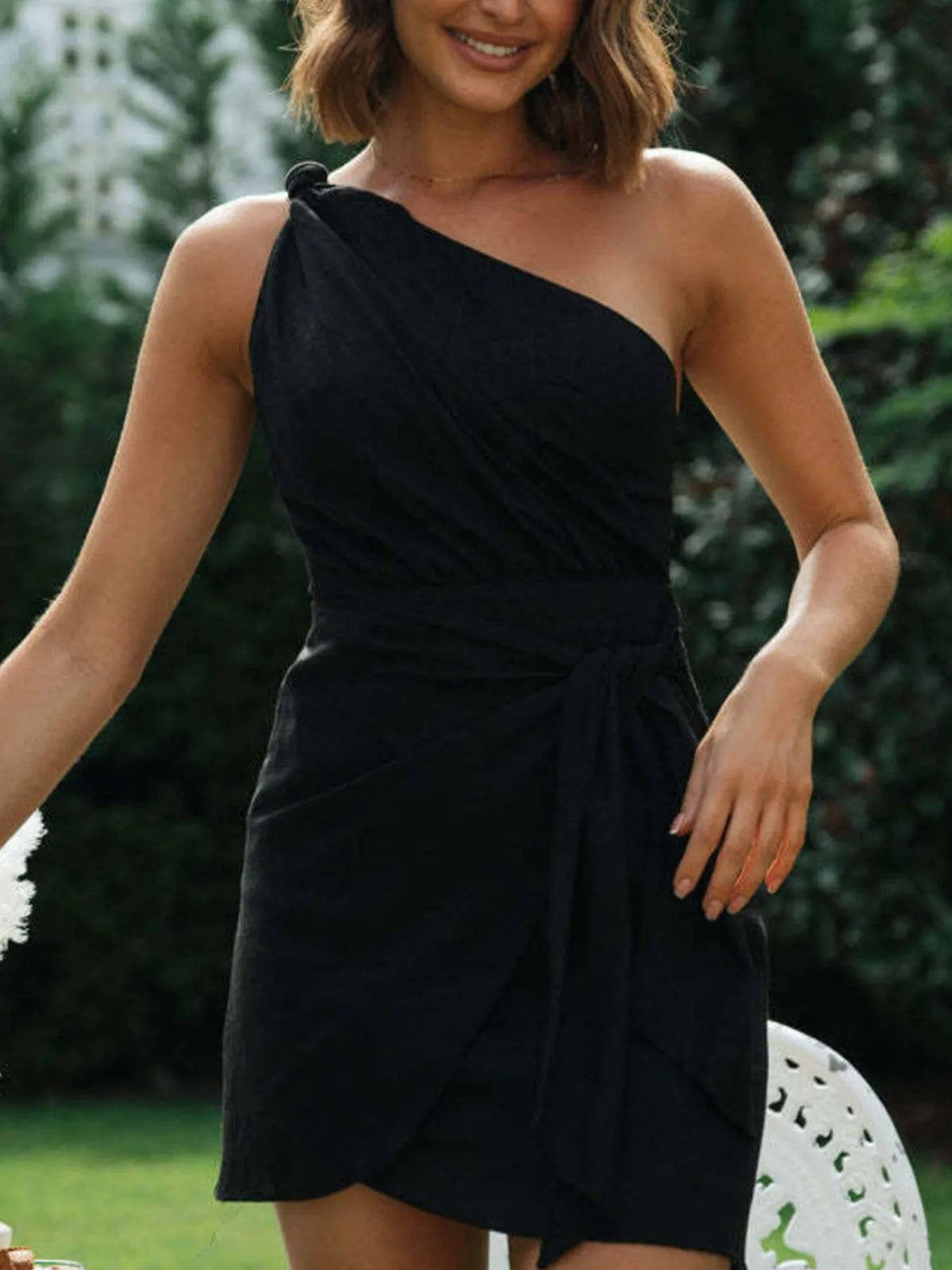 Model wearing the black dress, showing its draped asymmetrical neckline