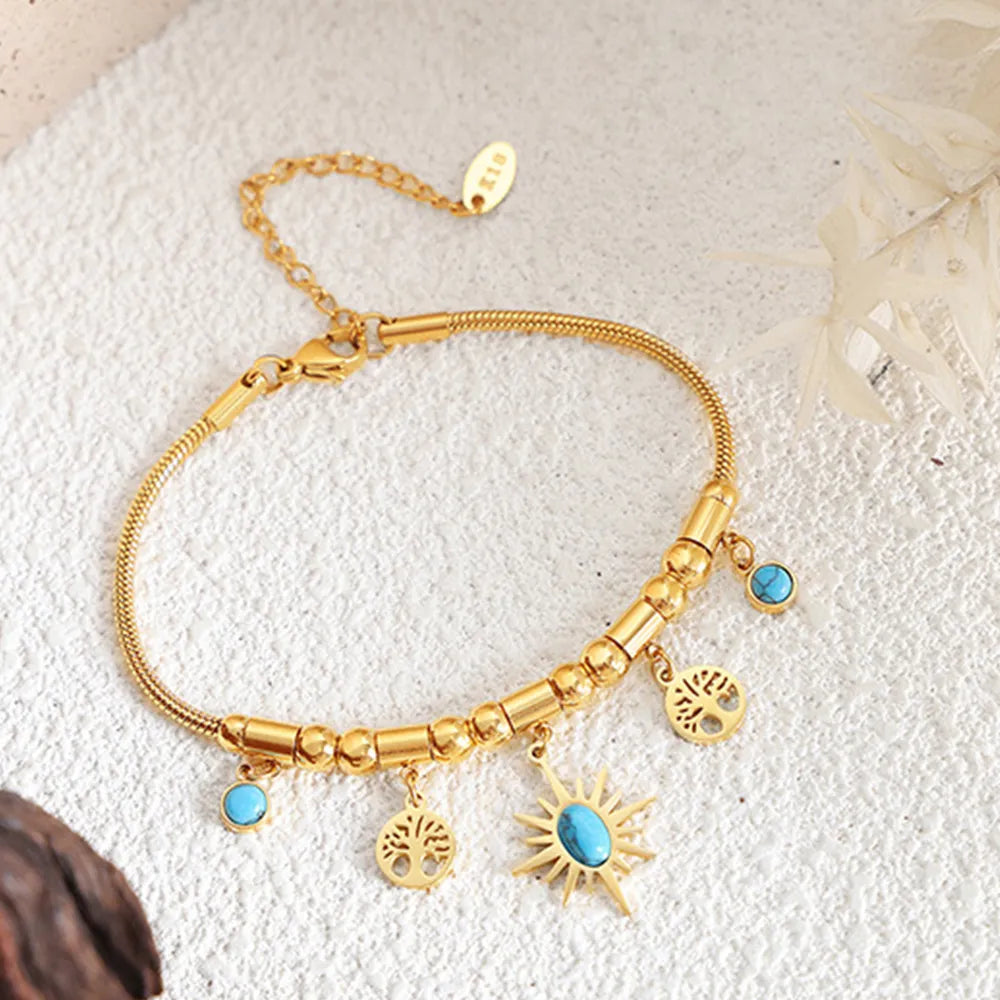 Gold bracelet with dangling sun and round charms laid flat
