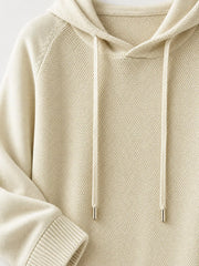 Cream sweater detail showing the knit texture, hood opening and metal-tipped drawstrings.