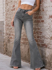 Grey high-waisted flare jeans with studded outer seams styled with a white crop top by a brick wall