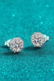 Round moissanite stud earrings at an angle on teal background