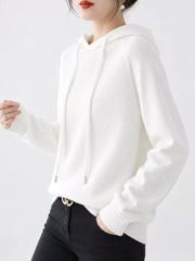 Angled view of the white knit sweater with one hand in a black trouser pocket.