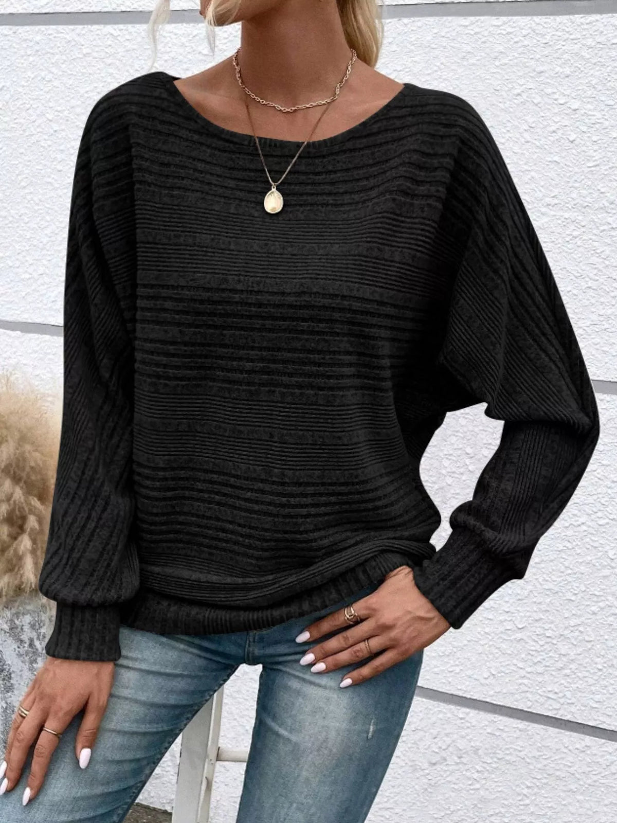 Women’s ribbed round-neck long-sleeve top in black front view with hand at hip
