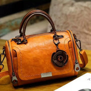 Tan flap crossbody bag with flower ornament shown from the front
