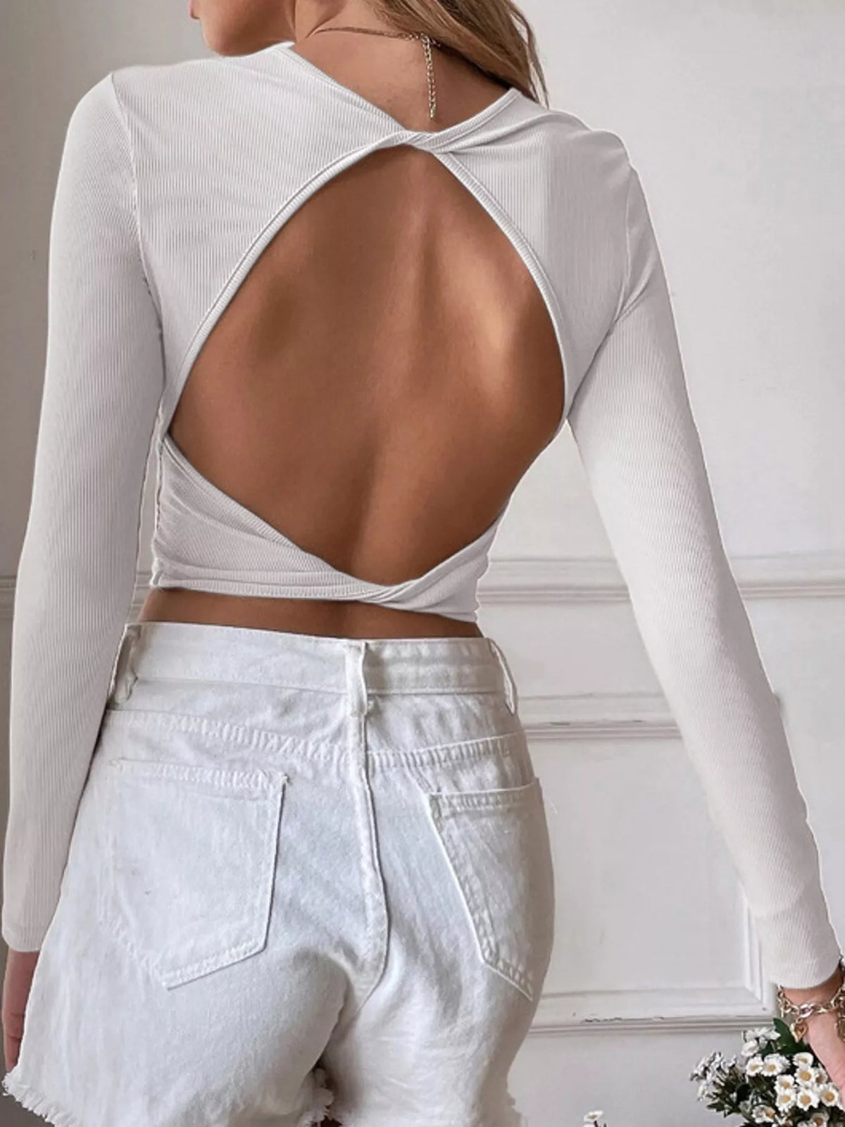Back view of a white long-sleeve crop top with a large open-back cutout