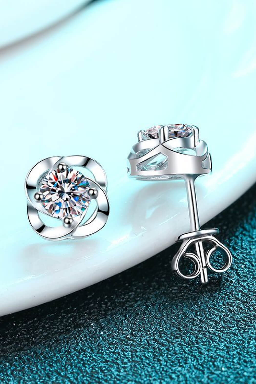 Silver-tone stud earrings on a pale dish showing a clear stone and butterfly back