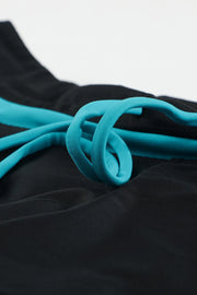 Close-up of the turquoise drawstring loop and stripe against black swim shorts.