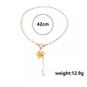Pearl choker with gold flower pendant and dangling pearl, worn with a floral top