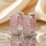 Silver-tone square hoop earrings with pink stones on reflective surface