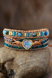 Colorful layered stone bracelet with a blue heart centerpiece displayed on a rock.