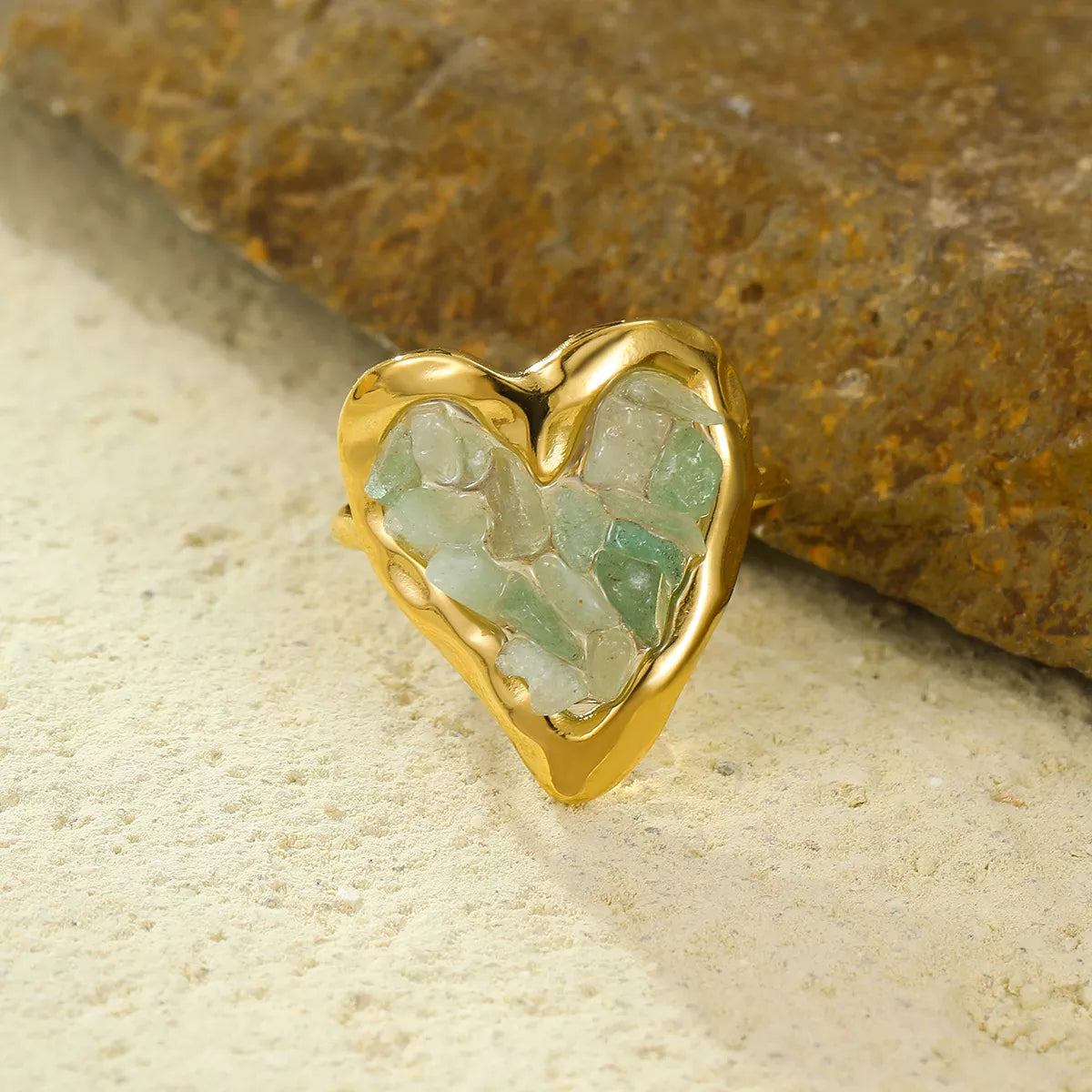 Gold-plated heart ring with pale pink stones resting on a textured surface