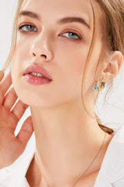 Model wearing gold-tone drop earrings with a white collared top