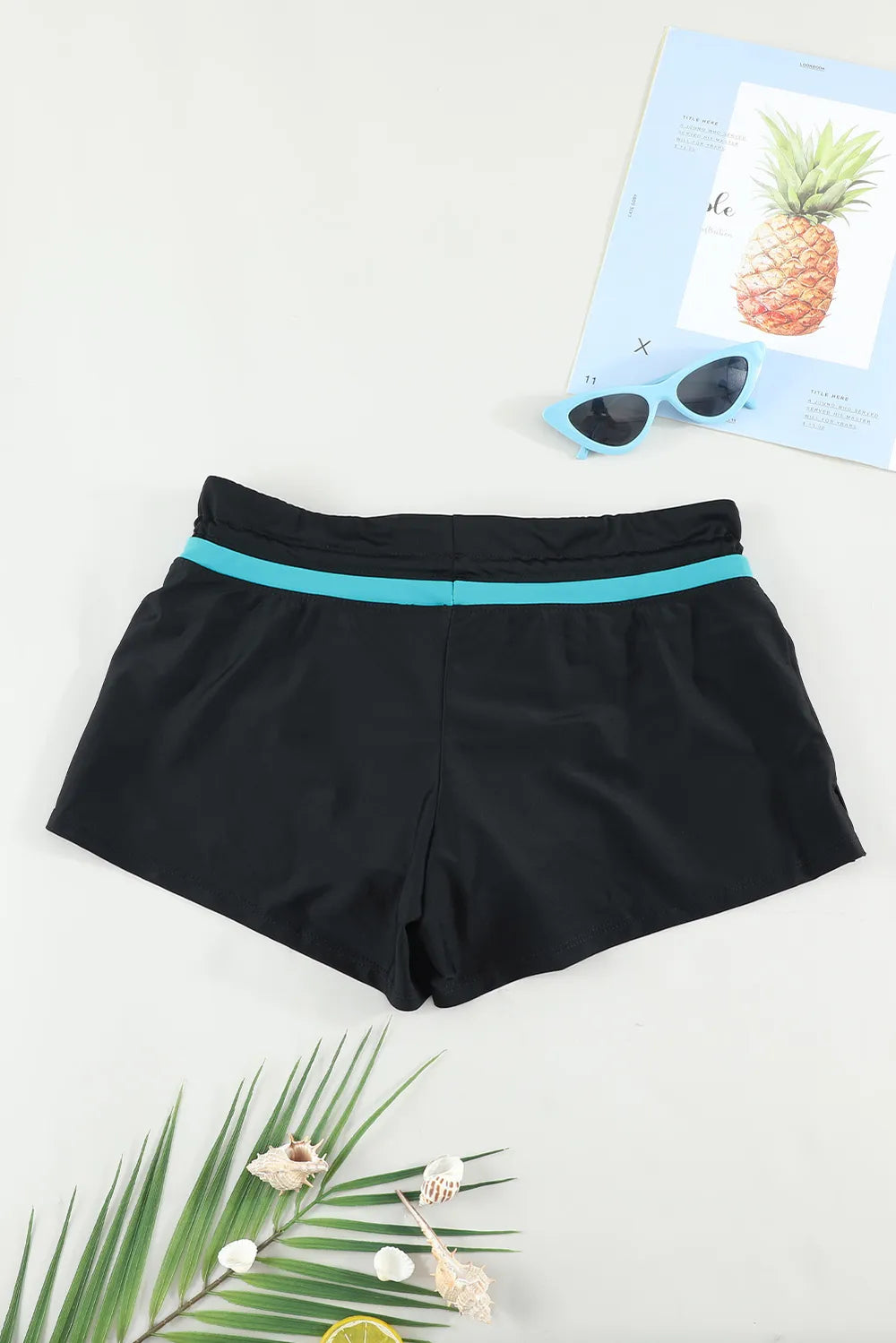 Back view of black swim shorts with a turquoise waistband stripe, laid flat.