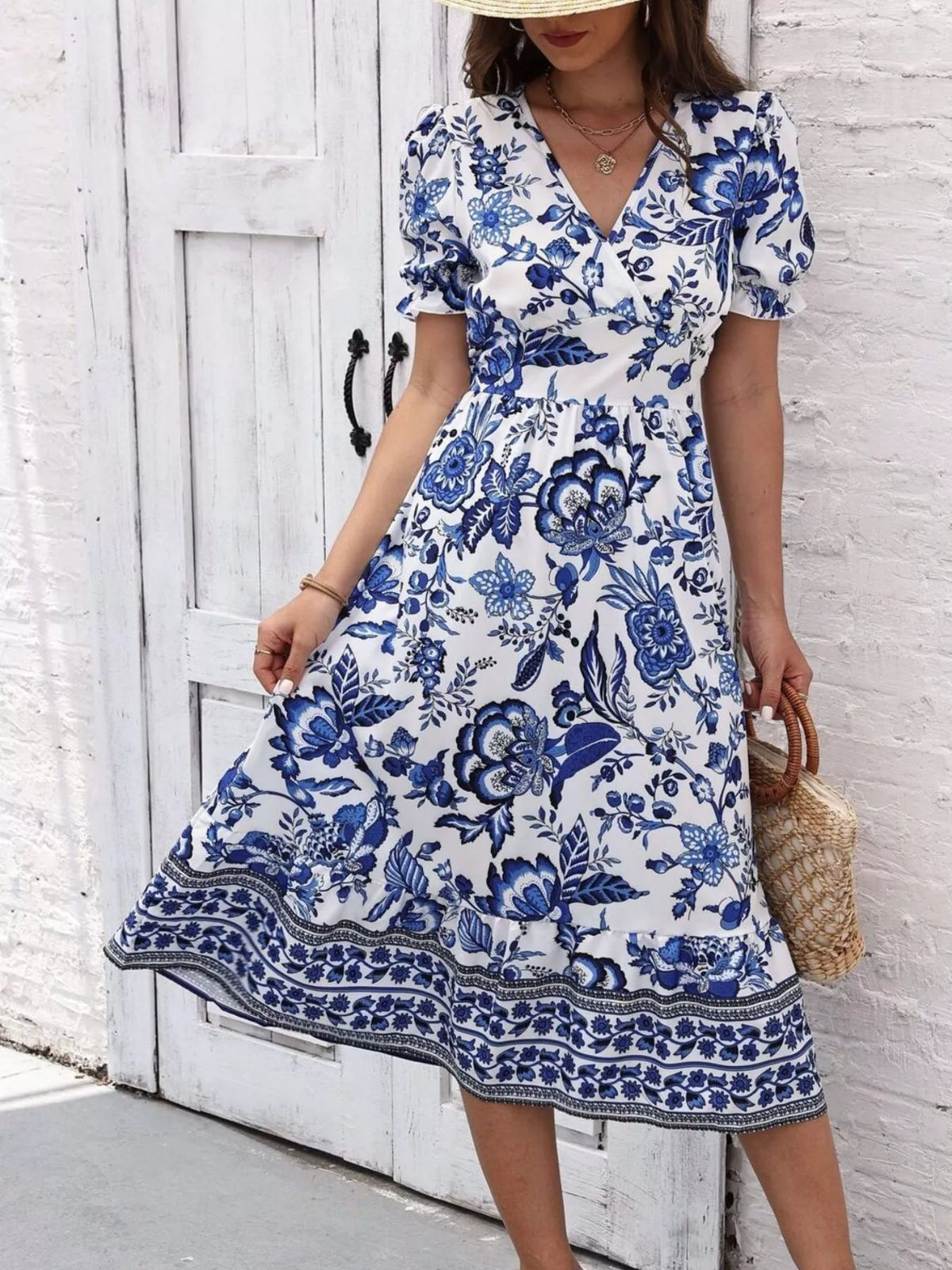 Blue floral midi dress with short puff sleeves and a border-print hem, shown holding one side of the skirt.