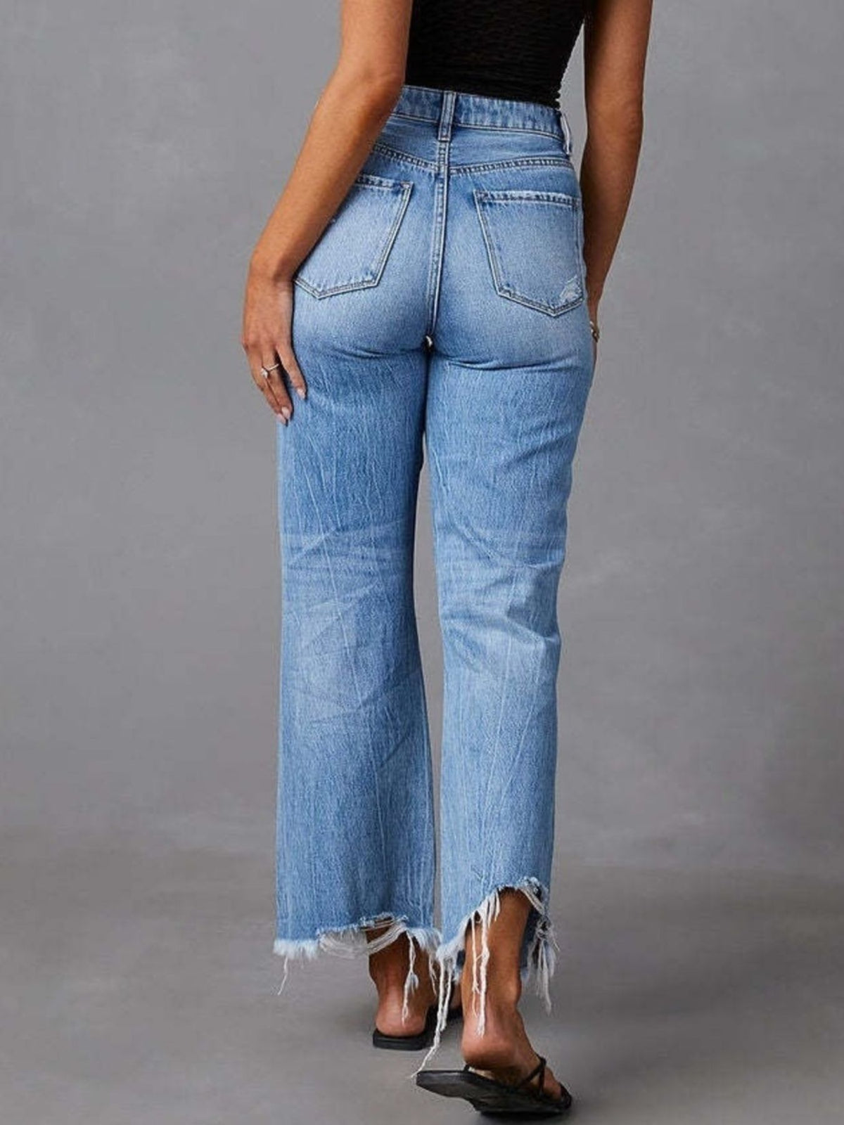 Back view of blue flare jeans with distressed details and raw hems.