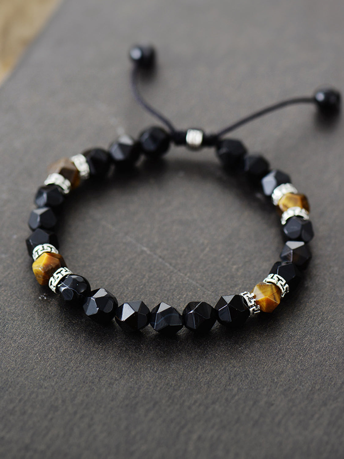 Black faceted bead bracelet with brown stone accents and patterned spacers on dark gray