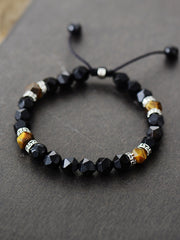 Black faceted bead bracelet with brown stone accents and patterned spacers on dark gray