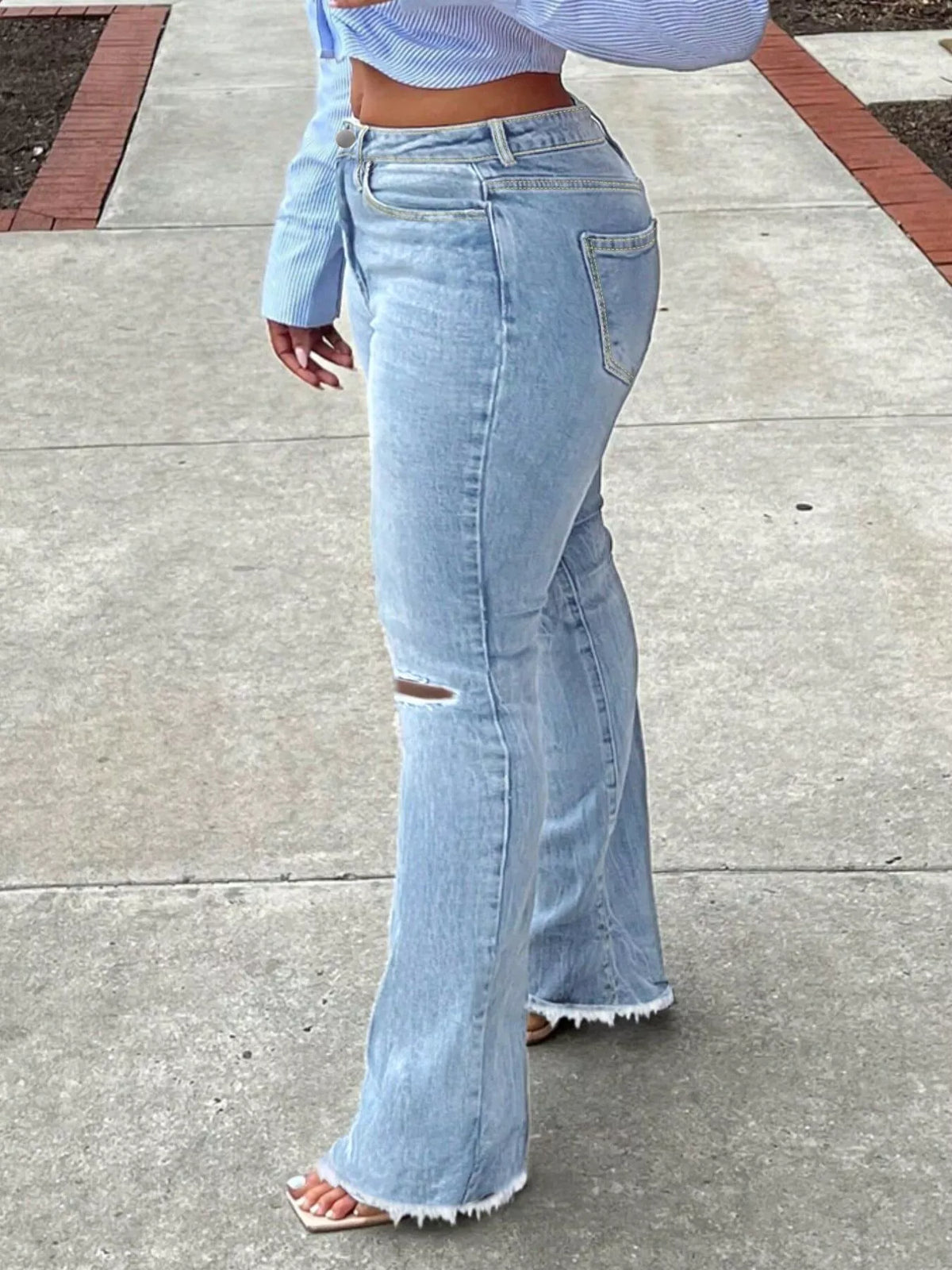 Side view of light blue ripped-knee jeans with flared legs and raw hems.