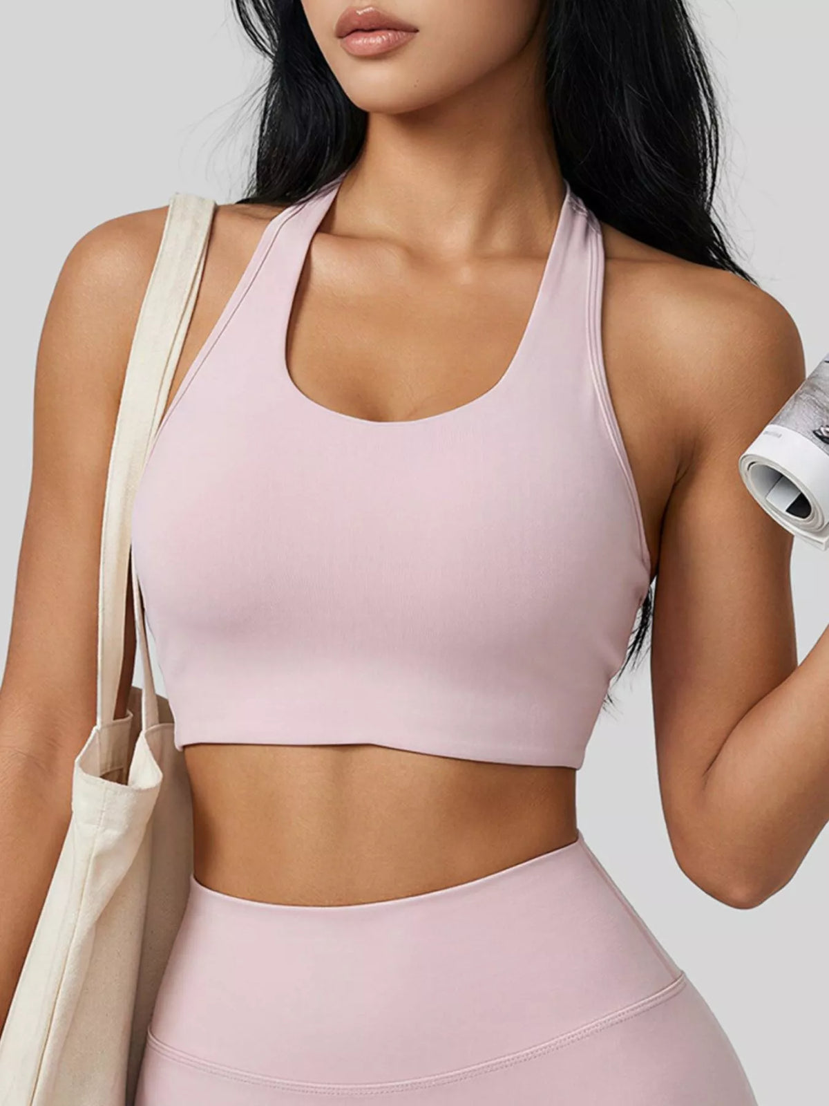 Front view of the pale pink halter active bra, styled with matching leggings and a tote.