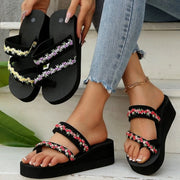 Black platform sandals with red floral-trim straps worn while yellow- and purple-trimmed pairs are held
