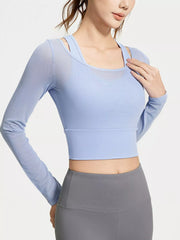 Model wearing a light blue long-sleeve cropped active top with inner bra straps visible at the scoop neckline