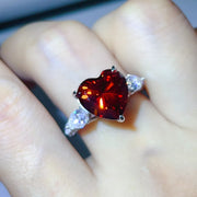 Deep red heart-shaped moissanite ring worn on a hand.