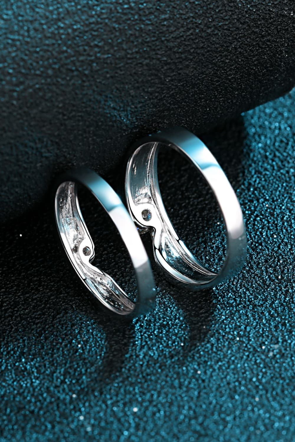 Two moissanite rings shown side by side against a dark teal surface.