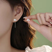 Lotus-shaped silver stud earrings with long dangling bar, worn on ear