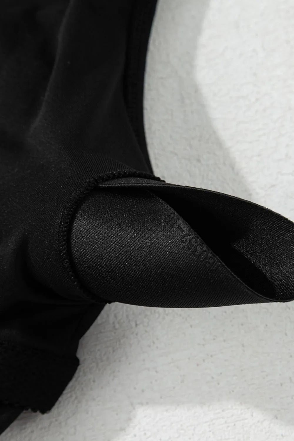 Close-up of the black swim dress strap hardware and gathered bodice seam.
