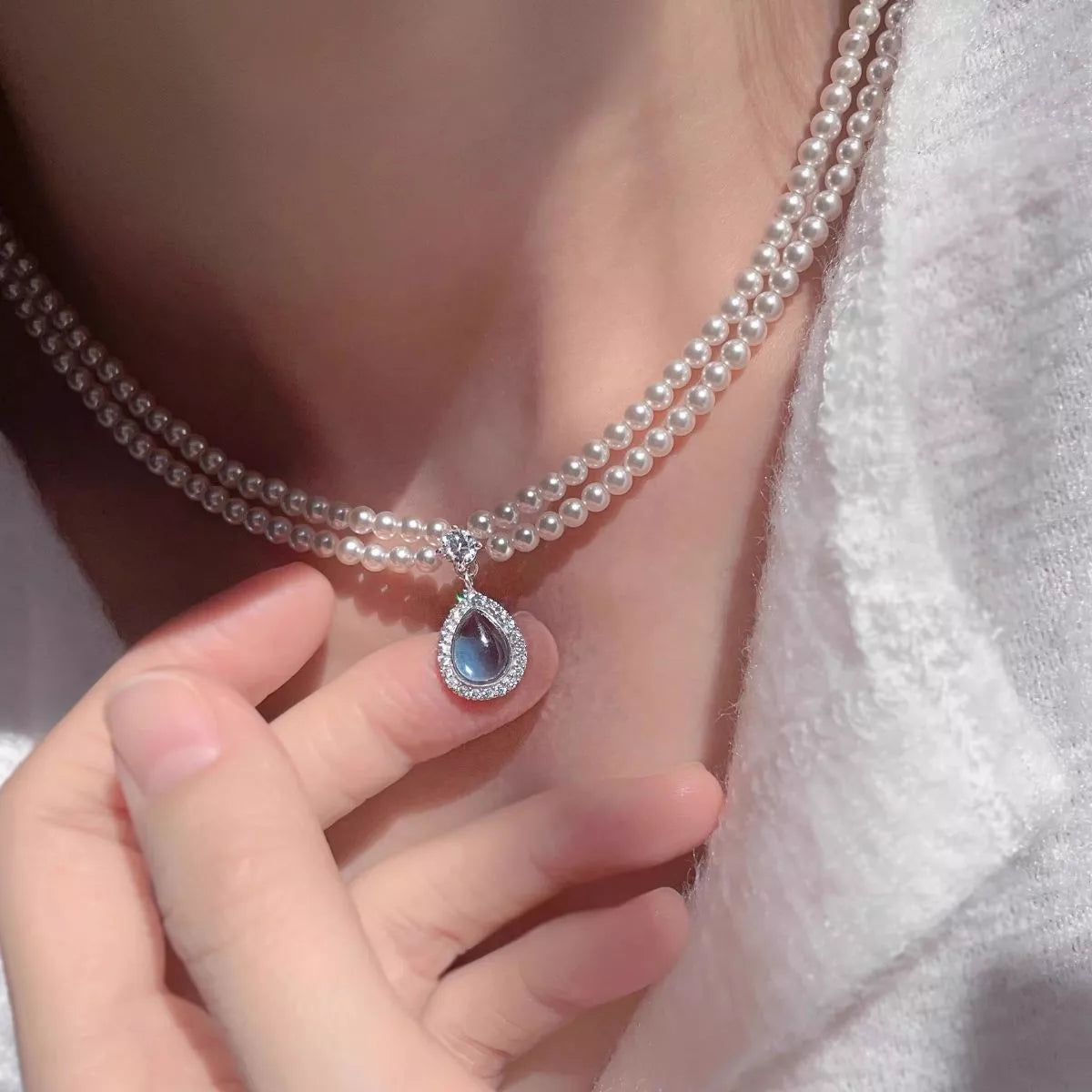Close-up of blue teardrop pendant on layered pearl necklace