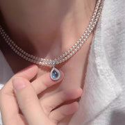 Close-up of blue teardrop pendant on layered pearl necklace