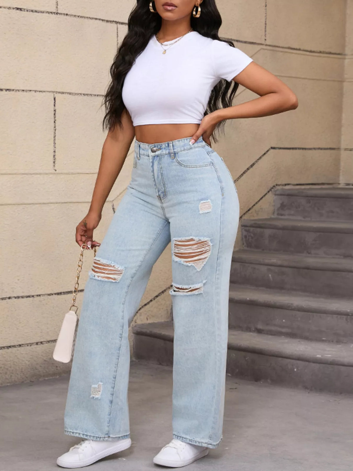 Angled full-length view of light-wash ripped jeans with a hand on the hip