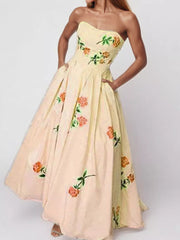 Model wearing a pale peach strapless maxi dress with multicolor floral embroidery.