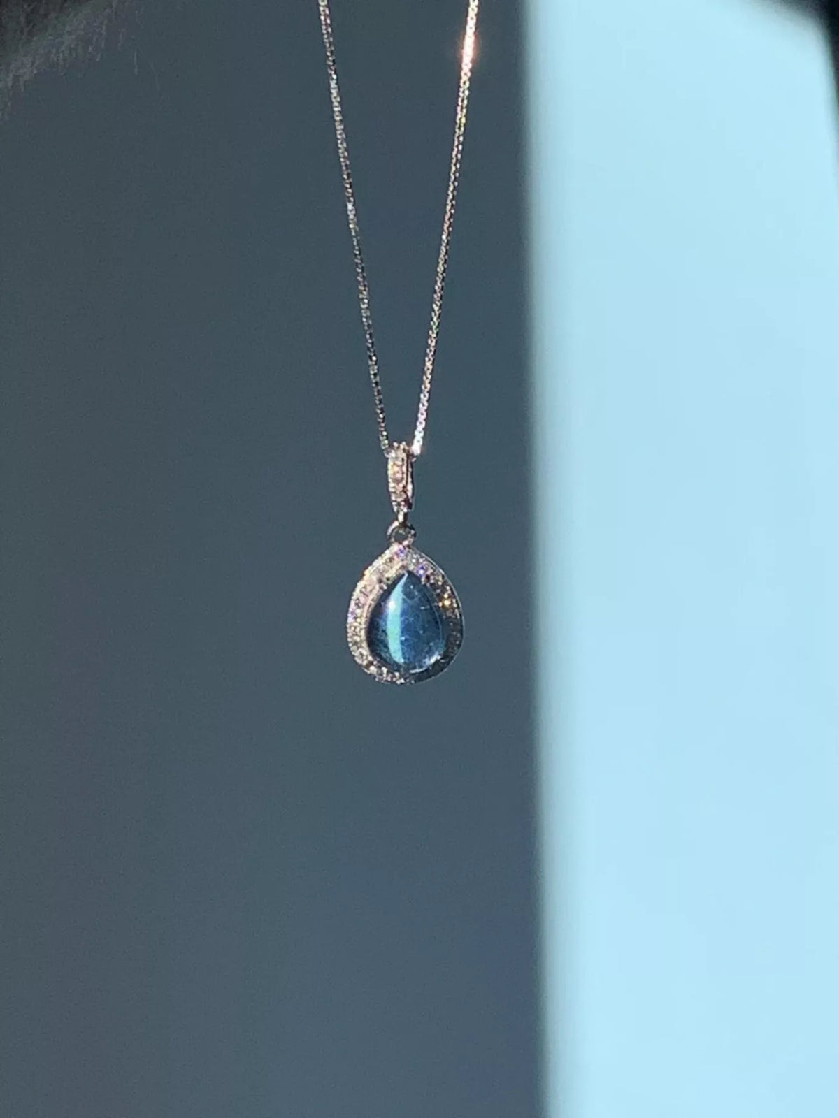 Blue teardrop crystal pendant hanging from a fine chain on blue backdrop