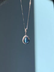 Blue teardrop crystal pendant hanging from a fine chain on blue backdrop