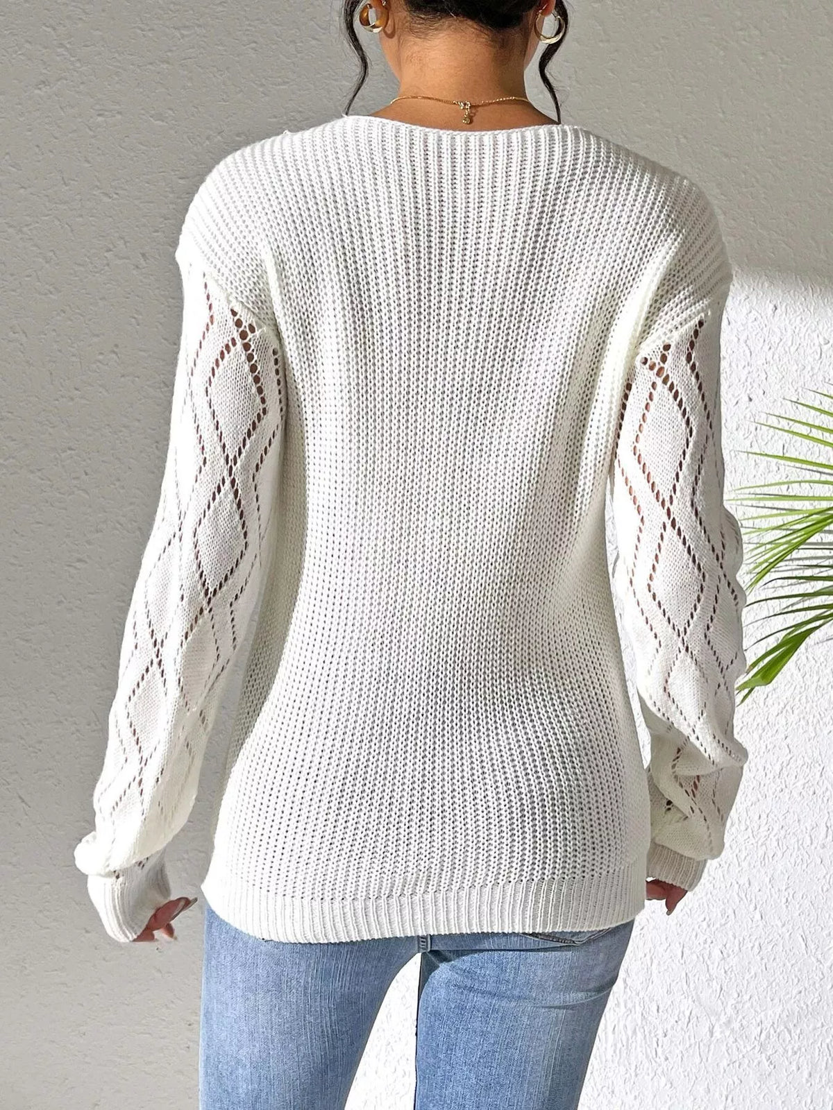 Back view of the white sweater showing its plain knit body and openwork sleeves.