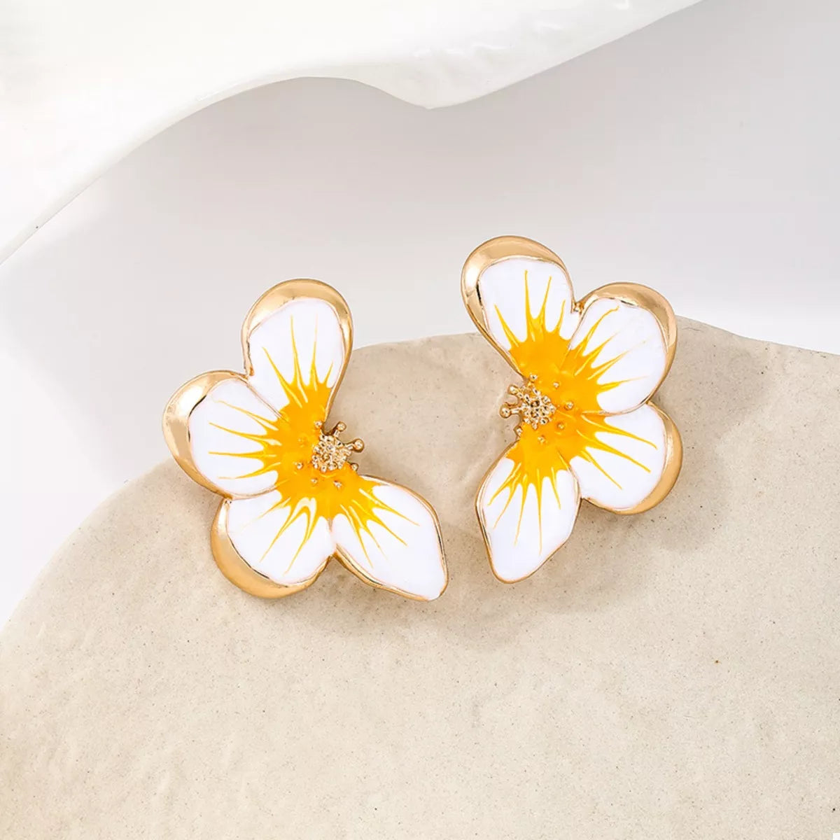 Pair of yellow-and-white flower studs resting on a pale stone