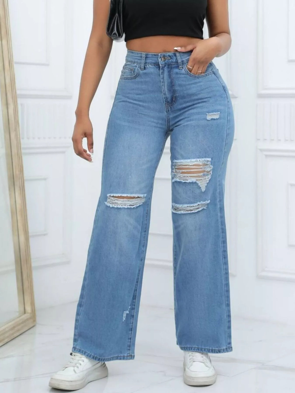 Front view of medium-blue ripped wide-leg jeans styled with a black top and white trainers