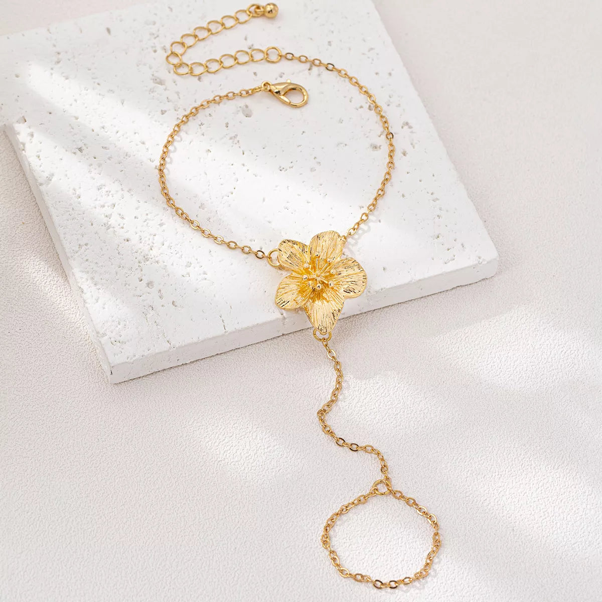 Gold-tone flower hand chain bracelet laid on a white jewelry box
