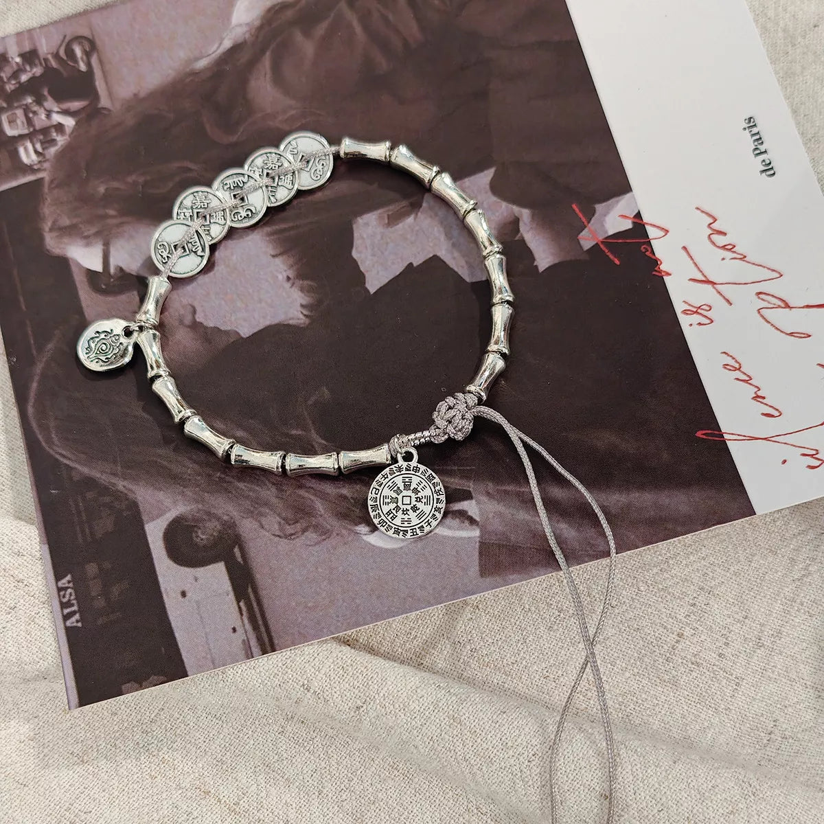 Silver-tone bracelet with circular charms and textured links displayed on a dark printed card.