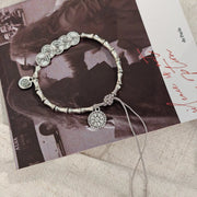 Silver-tone bracelet with circular charms and textured links displayed on a dark printed card.
